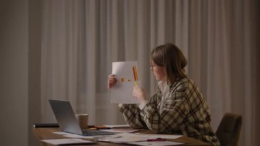 Uzaktan kumandalı gözlüklü genç bir kadın evde oturmuş online bir rapor hazırlarken dizüstü bilgisayarında grafikler gösteriyor. Program gösterisiyle görüntülü arama ve konferans