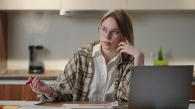 Gözlüklü bir kadın, mali belgeler üzerinde çalışıyor, iş yerinde dizüstü bilgisayar başvurusu ile oturuyor, odaklanmış görünüyor, bir görevi tamamlıyor, verimli bir iş günü raporunu hazırlıyor ve kontrol ediyor..