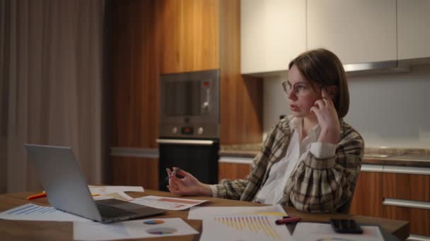 En lyhörd och trött kvinna med glasögon som arbetar med ekonomiska dokument, sitter på arbetsplatsen med hjälp av en laptop app, ser fokuserad ut när du slutför en uppgift. — Stockvideo