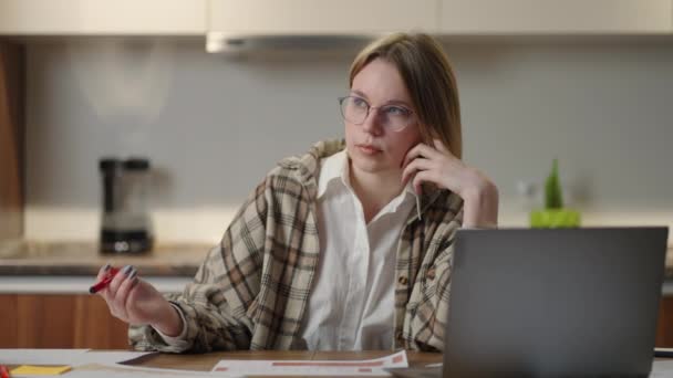 Gözlüklü bir kadın, mali belgeler üzerinde çalışıyor, iş yerinde dizüstü bilgisayar başvurusu ile oturuyor, odaklanmış görünüyor, bir görevi tamamlıyor, verimli bir iş günü raporunu hazırlıyor ve kontrol ediyor.. — Stok video