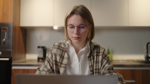 Zoom inverso Uma mulher com óculos trabalha remotamente em casa sentada a uma mesa com um laptop e uma caneta com ponta de feltro marca os dados no gráfico. Estudante de ensino à distância em casa para realizar uma tarefa — Vídeo de Stock