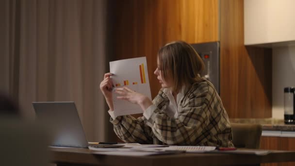 A young woman with glasses at home shows a graph Video call and conference with demonstration and analysis of documents and schedules. — Stockvideo