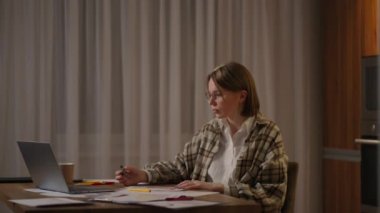 Gözlüklü bir kadın bilgisayarlı bir ofiste uzaktan çalışıyor ve grafikle ilgili verileri not ediyor, iş ekonomisti