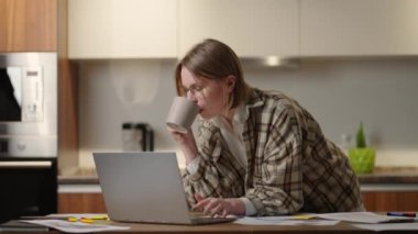 Sosyal medyada gezinirken sıcak çikolatanın tadını çıkaran güzel bir kadın evdeki kanepede rahatça oturuyor.