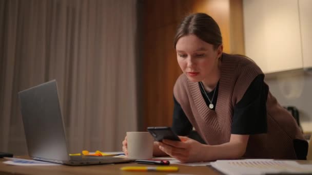 Žena pracující z domova, obchodní žena pracující na notebooku a používající mobilní telefon, která ráno popíjí kávu, sedí na stole v zahradě. Životní styl ženy pracující doma koncept. — Stock video