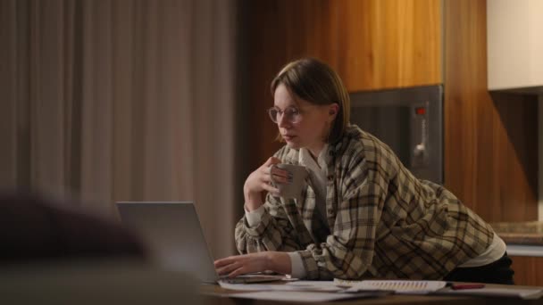 Une jeune femme d'affaires magnifique travaille de la maison avec une tasse de café et regarde dans un écran d'ordinateur portable debout à la table. Voir le courrier et boire du café. Travail à distance depuis la maison — Video