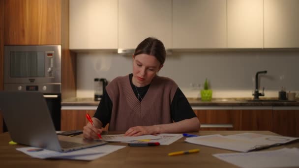 女性は書類を見て、テーブルの上のグラフは論文にメモを取ります。疲れた女が家から働いている。距離学習分析と計画 — ストック動画