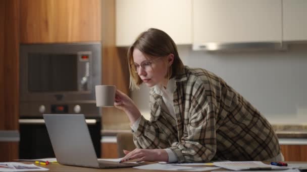 Una mujer bebe café y mira su portátil mirando los documentos — Vídeos de Stock