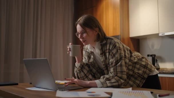 Beautiful young woman working on laptop computer while sitting at the living room, drinking coffee. Happy casual beautiful woman working on a laptop. working at home with laptop and documents — Stock videók