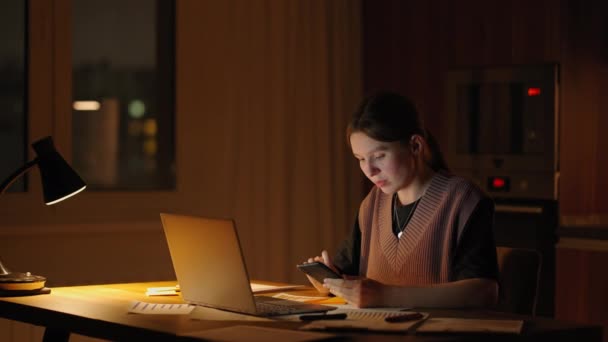 Beautiful woman working late at home using a laptop and receiving text messages on smartphone. Hands of woman texting message on mobile smart phone for communication and chatting on social online — Stock videók