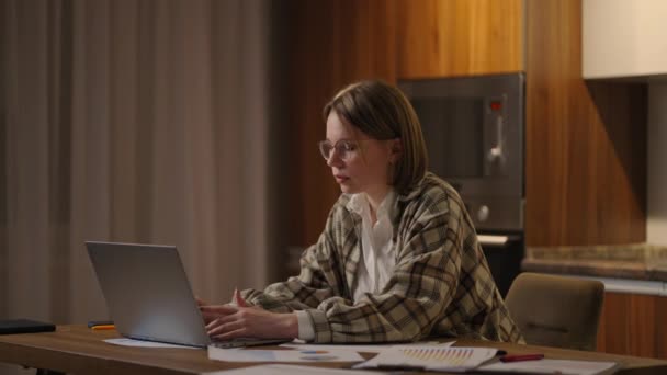 A girl works from home or a student is studying from home or a freelancer. She uses a laptop and a phone. girl sit at desk in living room study on laptop making notes, concentrated young woman work — Vídeo de Stock