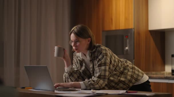 Beautiful young woman working on laptop computer while sitting at the living room, drinking coffee. Happy casual beautiful woman working on a laptop. working at home with laptop and documents — Vídeo de Stock