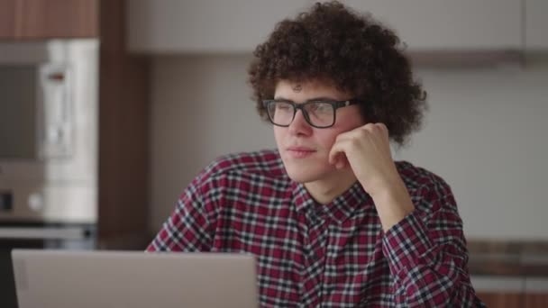 Brooding serious curly freelancer man sit at table in comfortable home office room work on laptop looks concentrated thinking over business issue solution, makes telecommute job — Stock Video