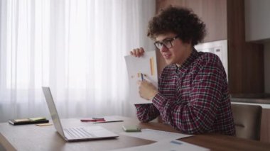 Kıvırcık saçlı, gözlüklü, ofis masasında oturan, kameraya bakan ve grafiksel form grafiği olan bir tableti işaret eden bir iş adamı.