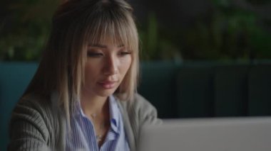 Ofisteki ahşap masaya yerleştirilmiş kahve ve dizüstü bilgisayarlı güzel, gülümseyen Asyalı iş kadını. Evden işe giderken e-postaları kontrol eden ya da araştırma yapan kadın