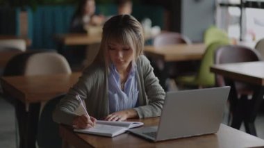 Ofisteki ahşap masaya yerleştirilmiş kahve ve dizüstü bilgisayarlı güzel, gülümseyen Asyalı iş kadını. Evden işe giderken e-postaları kontrol eden ya da araştırma yapan kadın