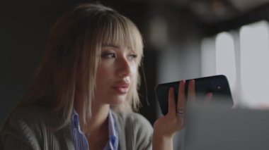 Asyalı kadın cep telefonunda ses asistanı kullanarak konuşuyor. Kanepede oturan kadın, arkadaşıyla telefonda konuşuyor. Ses tanıma ya da istek sanal asistanı aracılığıyla internet hizmetleri kullanıyor.