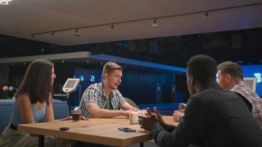 A multi ethnic group of friends in a bowling club communicate at the table and rejoice in the victory of a friend