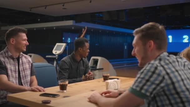 Група друзів в боулінг-клубі спілкуються за столом і радіють перемозі друга — стокове відео