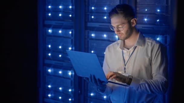 Man Server Engineer in het datacenter. IT-ingenieur inspecteert een beveiligde serverkast met behulp van moderne technologie laptop coworking in datacenter. — Stockvideo