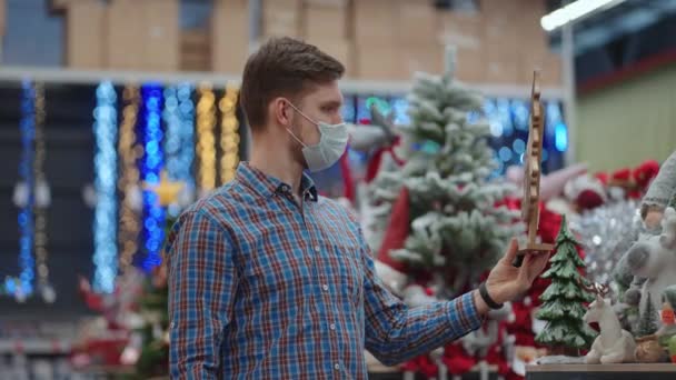 Shopping in pandemic and quarantine. A man in a protective mask in a jewelry store and garlands with toys for Christmas trees and at home. Christmas garlands and decor. — Stockvideo