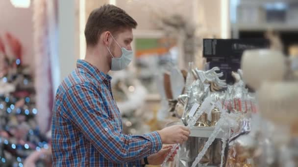 A man in a protective mask in a jewelry store and garlands with toys for Christmas trees and at home. Christmas garlands and decor — Vídeo de Stock