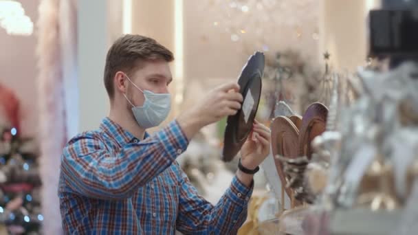 A man in a protective mask in a jewelry store and garlands with toys for Christmas trees and at home. Christmas garlands and decor — Vídeo de Stock