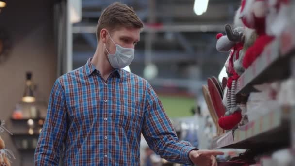 A man in a protective mask in a jewelry store and garlands with toys for Christmas trees and at home. Christmas garlands and decor — Wideo stockowe