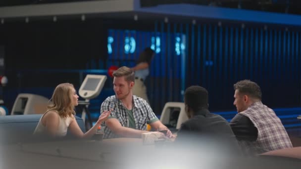 A multi ethnic group of friends in a bowling club are chatting at the table and smiling, rejoicing and high-fiving a friend who knocked out a strike — 图库视频影像