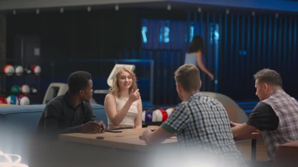 A multi-ethnic group of friends in a bowling club are chatting at the table and smiling, rejoicing and high-fiving a friend who knocked out a strike. Black man and woman — 图库视频影像