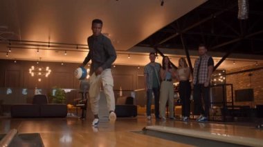Multi ethnic Group of friends in a bowling club a black man throws a ball and knocks out a strike