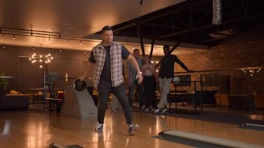 A Caucasian young man makes a throw in a bowling club and enjoys emotionally knocking out pins with a ball