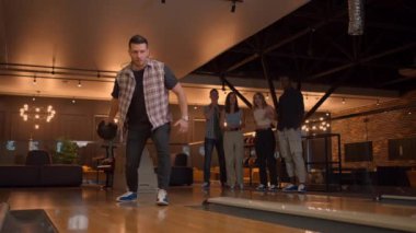 Multi ethnic Group of friends in a bowling club Caucasian man throws a ball and knocks out a strike