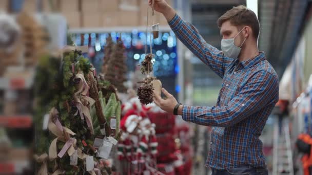 Shopping in pandemic and quarantine. A man in a protective mask in a jewelry store and garlands with toys for Christmas trees and at home. Christmas garlands and decor. — Stockvideo