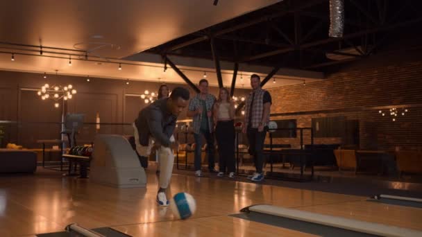 A black man makes a throw in a bowling club and enjoys emotionally knocking out pins with a ball — стоковое видео