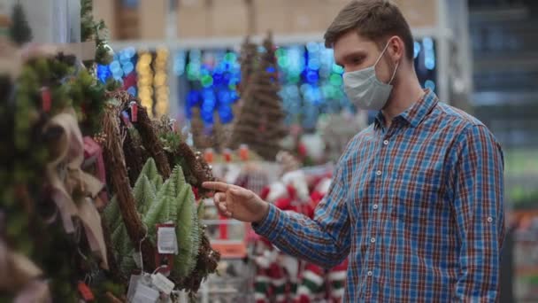 A man in a protective mask in a jewelry store and garlands with toys for Christmas trees and at home. Christmas garlands and decor — Wideo stockowe