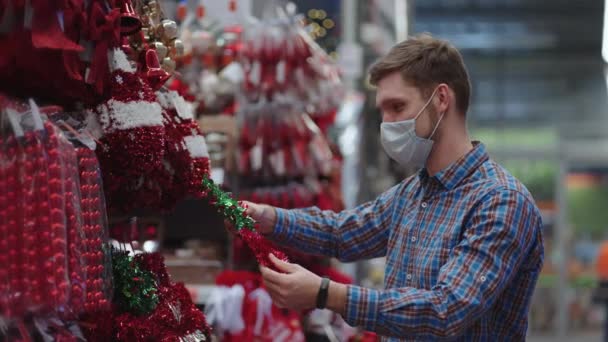 A man in a protective mask in a jewelry store and garlands with toys for Christmas trees and at home. Christmas garlands and decor — ストック動画