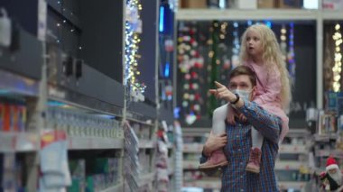 dad and daughter choose decorations and garlands with toys for Christmas trees and at home in the store. Christmas garlands and decor