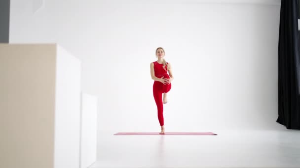 Beautiful young woman wearing red sportswear doing yoga or pilates exercise pose, on white background. — Stok video