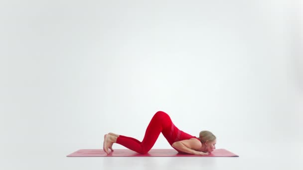 Beautiful young woman wearing red sportswear doing yoga or pilates exercise pose, on white background. — Stock Video
