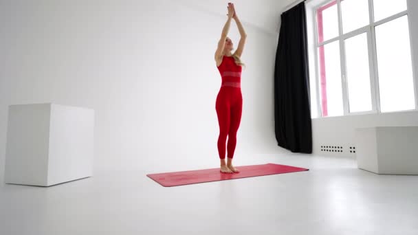 Beautiful young woman wearing red sportswear doing yoga or pilates exercise pose, on white background. — Stockvideo