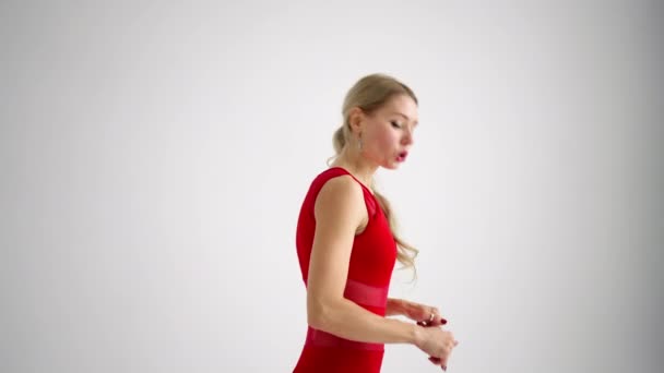 A woman in a red tracksuit looking into the camera conducts training and tells and shows exercises from yoga or Pilates on a white background. Yoga instructor shows exercises for home classes — Vídeo de Stock