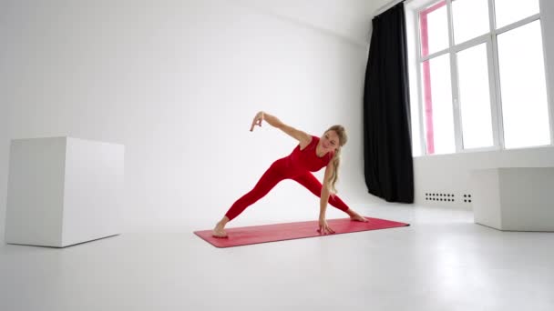 Young attractive girl practicing yoga isolated on white background in red Sportswear . Concept of healthy life and natural balance between body and mental development. Full length — ストック動画