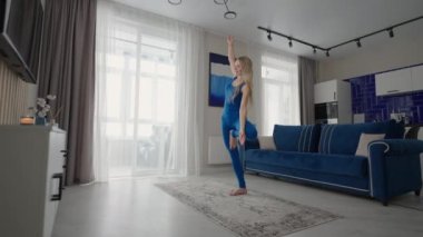 Young Woman Meditating Sitting on Carpet and Doing Splits stretching, Doing Yoga, Blue Sportswear Light Room At Home In the Morning. woman practicing yoga at home