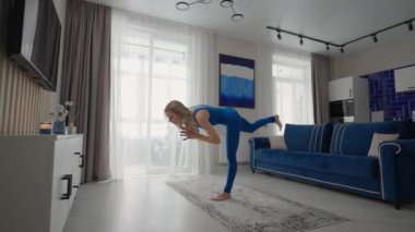Young Woman Meditating Sitting on Carpet and Doing Splits stretching, Doing Yoga, Blue Sportswear Light Room At Home In the Morning. woman practicing yoga at home