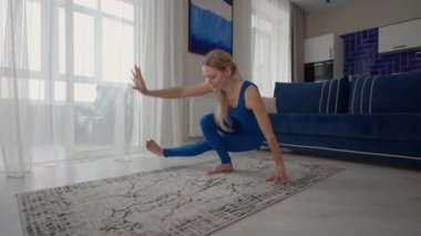 young woman is practising yoga at home relaxing in simple body position sitting on floor with beautiful furniture around. slim woman in sportswear standing on knees, bending back and doing camel pose