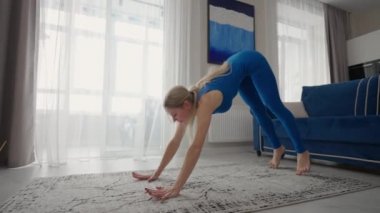 Young Woman Meditating Sitting on Carpet and Doing Splits stretching, Doing Yoga, Blue Sportswear Light Room At Home In the Morning. woman practicing yoga at home