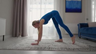 young woman is practising yoga at home relaxing in simple body position sitting on floor with beautiful furniture around. slim woman in sportswear standing on knees, bending back and doing camel pose