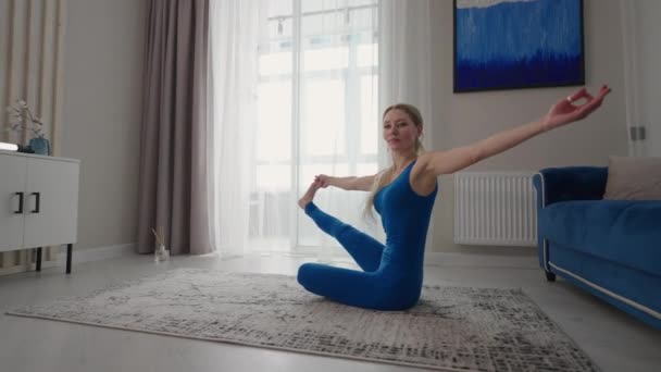 Mujer joven está practicando yoga en casa relajándose en posición corporal sencilla sentada en el suelo con hermosos muebles alrededor. mujer delgada en ropa deportiva de pie sobre las rodillas, inclinándose hacia atrás y haciendo pose de camello — Vídeos de Stock