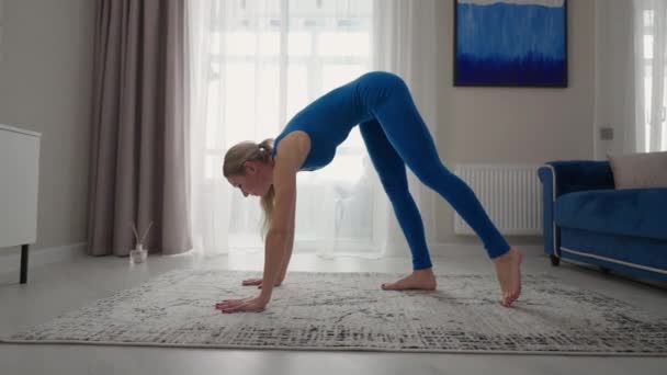 Mujer joven está practicando yoga en casa relajándose en posición corporal sencilla sentada en el suelo con hermosos muebles alrededor. mujer delgada en ropa deportiva de pie sobre las rodillas, inclinándose hacia atrás y haciendo pose de camello — Vídeos de Stock